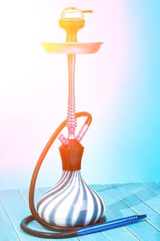 Modern hookah on light blue background. Eastern smokable water pipe smoking. Hookah with black rubber tube and blue and white flask on light blue background. Still life. Sun flare