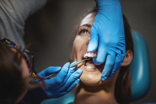 The beautiful young woman is at the dentist. She sits in the dentist's chair and the dentist sets braces on her teeth putting aesthetic self-aligning lingual locks.