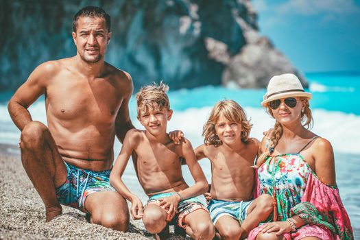 Young family with two sons are posing on the sea beach in summer day and looking at camera.