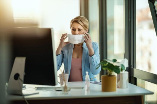 Business woman in a medical protective mask works at the office on the computer during self-isolation and quarantine to avoid infection during flu virus outbreak and coronavirus epidemic.