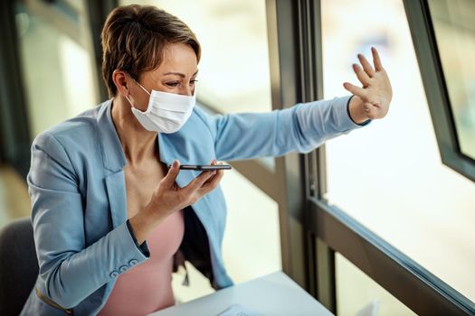 Business woman in a medical protective mask is working from home and using smartphone during self-isolation and quarantine to avoid infection during flu virus outbreak and coronavirus epidemic waving someone out the window.