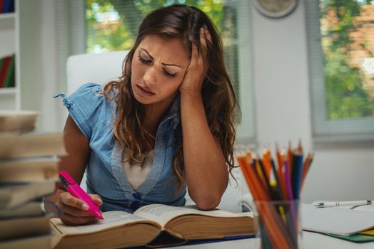 Beautiful tired young female student  with book is preparing exam and learning lessons in school library.