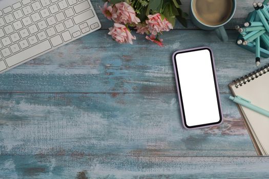 Above view smart phone with blank screen, coffee cup, notebook and stationery on wooden background. Copy space.