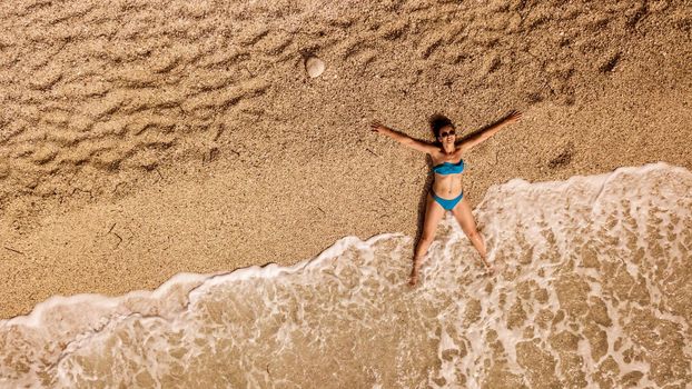 Aerial view of woman is relaxing on the beach by the sea. She is laying on the sandy beach and enjoying the sunbathing.