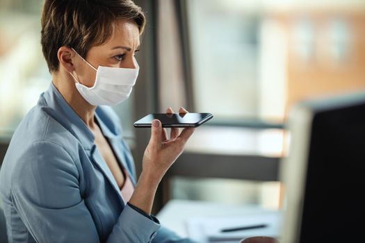 Business woman in a medical protective mask works at the computer and talking on a smartphone during self-isolation and quarantine to avoid infection during flu virus outbreak and coronavirus epidemic