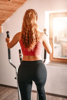 Rear view of a beautiful young woman exercising on stepper at home.