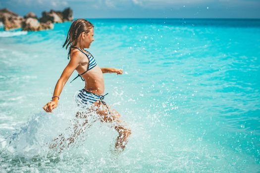 A little girl having fun in the waves of the sea and the drops of water are splashing all over her.
