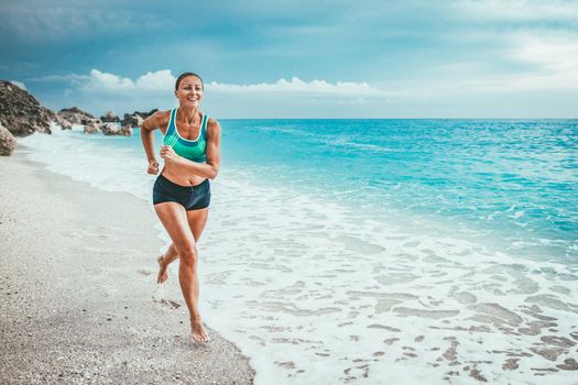 Beautiful young woman is running along the sea shore in the end of the day.