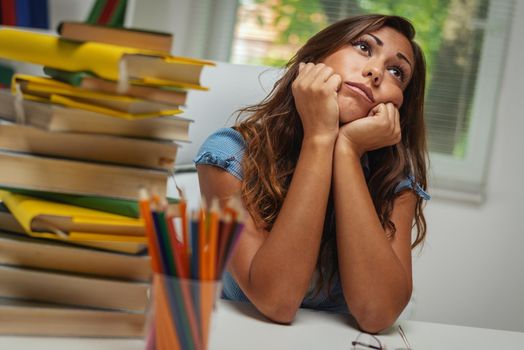 A beautiful bored young female student  with book is preparing exam and learning lessons in school library.