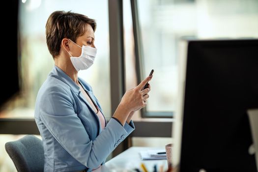 Business woman in a medical protective mask works from home at the computer, using smartphone, during self-isolation and quarantine to avoid infection during flu virus outbreak and coronavirus epidemic.
