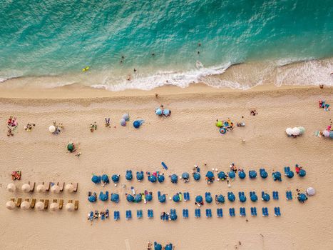Aerial view of the amazing beach with colorful umbrella and people who relaxing and swimming in clear water of Mediterranean sea at sunny day.