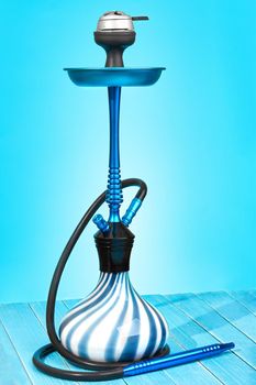 Modern hookah on light blue background. Eastern smokable water pipe smoking. Hookah with black rubber tube and blue and white flask on light blue background. Still life.