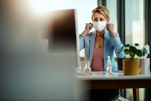 Business woman in a medical protective mask works at the office on the computer during self-isolation and quarantine to avoid infection during flu virus outbreak and coronavirus epidemic.