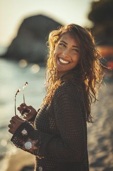 A beautiful young woman is having fun and relaxing on the beach at the sunset. 