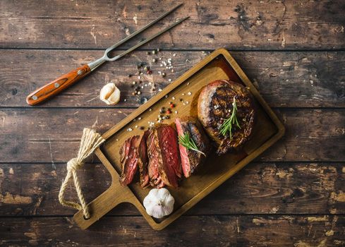 Sliced grilled marbled meat steak Filet Mignon, seasoning, fork, wooden cutting board. Juicy meat steak. Beef steak grilled/fried. Top view. Roasted meat steak. Close-up. Rustic. Concept, grilled meat