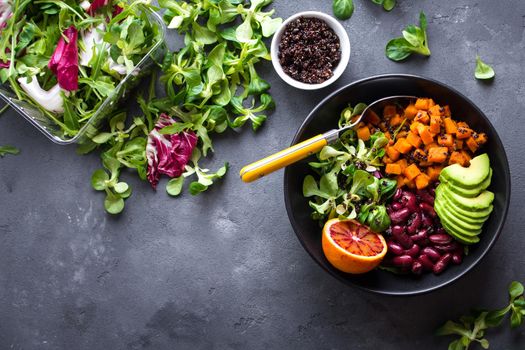 Quinoa salad in bowl with avocado, sweet potato, beans, herbs, orange on concrete rustic background. Quinoa superfood concept. Clean healthy detox eating. Vegan/vegetarian food. Making healthy salad