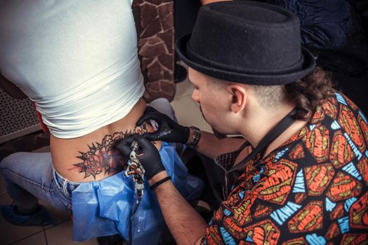 Skin master demonstrates the process of getting tattoo in tattoo parlour./Tattoo artist posing in tattoo studio.