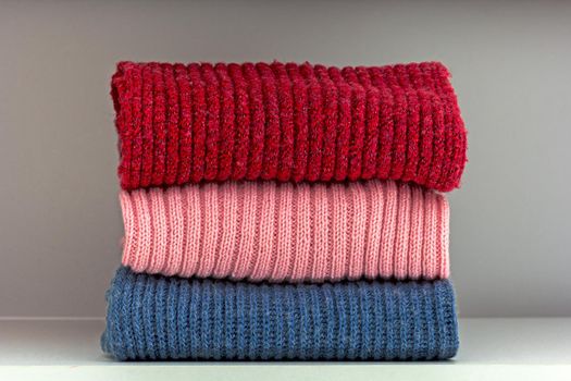 Stack of red, pink and blue wool cloth on shelf in white wardrobe