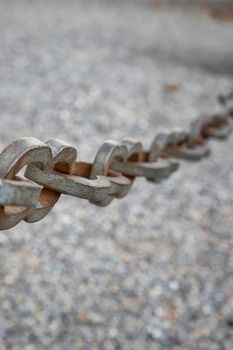 A light gray metal chain made of steel and showing its age is seen up close as it hangs above the broken stone ballast. Selective focus.Vertical view