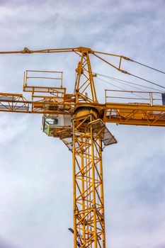 Construction tower crane, cabin, closeup, on blue sky with clouds. Vertical view