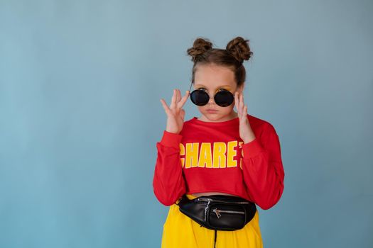 beauty portrait of stylish teenage girl in fashionable bright clothes. tween wearing red and yellow clothes on blue background. fashion portrait. two topknots. bright orange make up.