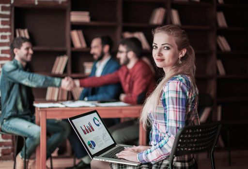 accountant works with financial charts on the laptop in the office on the background of business partners handshaking