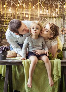 happy mother and father kissing their five year old daughter in the living room