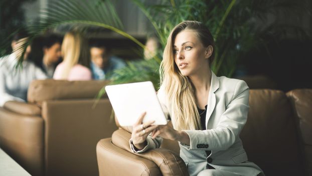 Successful business woman with a digital tablet sitting on the couch in the lobby of a modern office