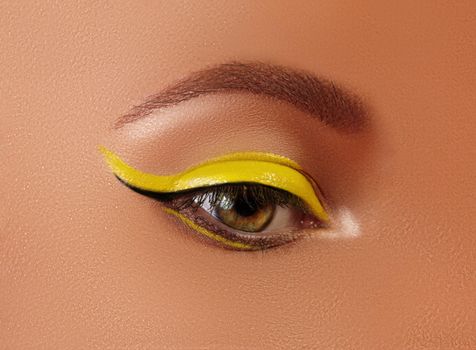 Beautiful macro close-up of female Eye with bright yellow Eyeliner Makeup. Neon Disco make-up and Fashion Manicure. Summer beauty styleCloseup macro shot of fashion liner eyes visage
