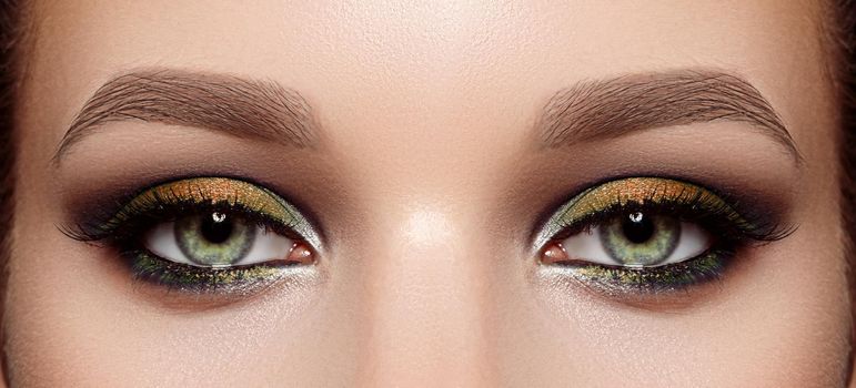 Closeup Macro of Woman Face with Green Eyes Make-up. Fashion Gold Autumn Makeup, Glowy Clean Skin, perfect Shapes of Brows. Shiny Shimmer. Beautiful Fall Trendy Colors in Make-up