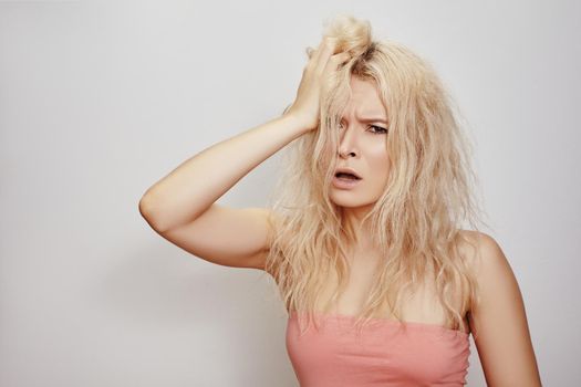 Bad hair day. Beautiful woman with messed up hair. Unhappy grimacing face. Blond bleaching hairstyle with problem brittle hair