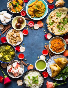 Festive food for Indian festival Diwali. Naan, samosa, rice, paneer, sweets. Background. Holiday Indian table with food, sweets, flowers, burning candles. Diwali celebratory dinner. Space for text.