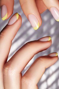 Hands with bright yellow french manicure on geometric background. Nails art design. Close-up of female hands with trendy neon nails on silver striped print