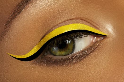 Beautiful macro close-up of female Eye with bright yellow Eyeliner Makeup. Neon Disco make-up with fashion black liner. Summer beauty style. Closeup macro shot of fashion liner eyes visage