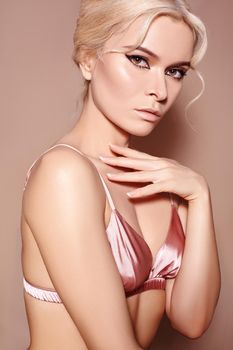 Beautiful sexy model with retro style make-up, clean skin, blond hair bun on beige background. Elegant woman model in pink lingerie in femininity pose with fashion make-up, hairstyle