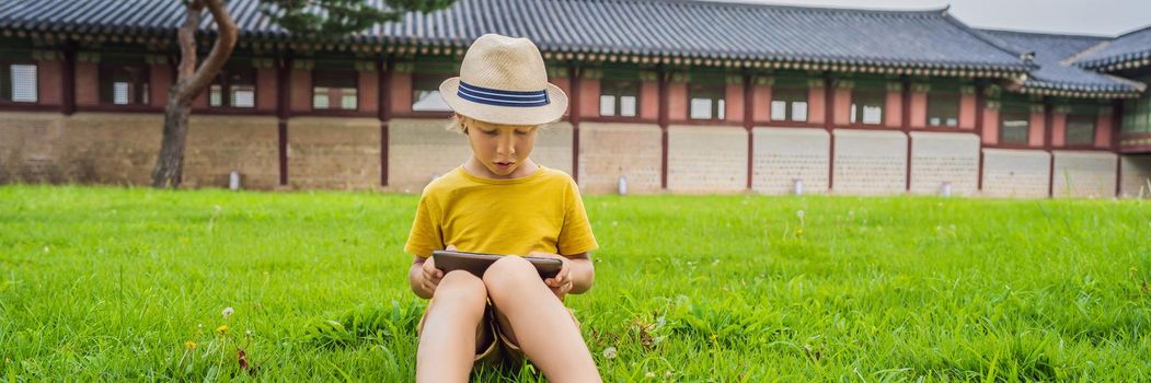 Young boy outdoors on the grass at backyard using his tablet computer. Educating and playing. BANNER, LONG FORMAT