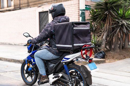 Food delivery driver with backpack on a motorcycle riding along a street