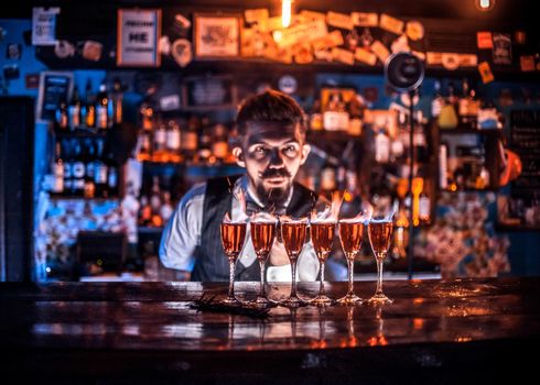 Expert bartender intensely finishes his creation while standing near the bar counter in nightclub
