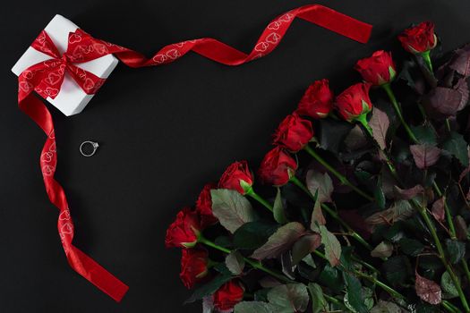 Red roses, ring and gift box on black background. Top view. Flat lay. Copy space. Still life