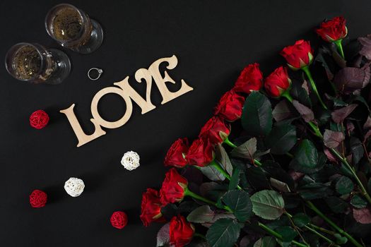 Bouquet of red roses and two glasses of champagne on a black background. Top view. Flat lay. Copy space. Still life