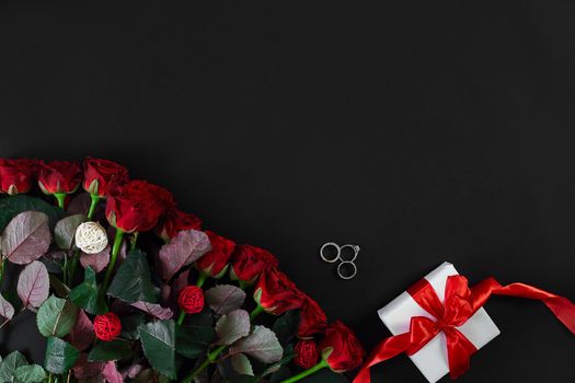 Red roses, ring and gift box on black background. Top view. Flat lay. Copy space. Still life