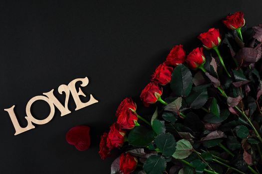 A bouquet of red roses and a box of ring on black background. View top. Flat lay. Copy space. Still life Valentine's Day