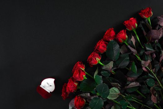 A bouquet of red roses and a box of ring on black background. View top. Flat lay. Copy space. Still life Valentine's Day