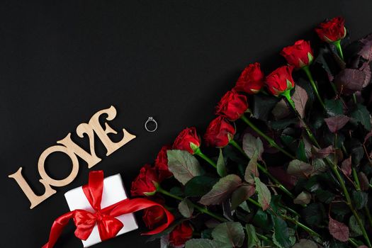 Red roses, ring and gift box on black background. Top view. Flat lay. Copy space. Still life