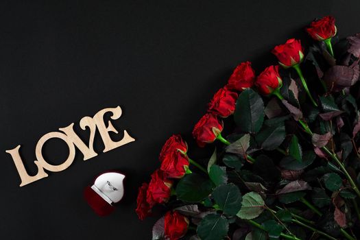 A bouquet of red roses and a box of ring on black background. View top. Flat lay. Copy space. Still life