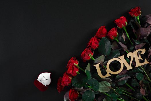 A bouquet of red roses and a box of ring on black background. View top. Flat lay. Copy space. Still life