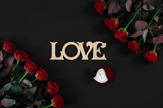 Red roses flowers with wooden word LOVE on black background with place for text. Romantic Valentines holidays concept. Valentine's day greeting card.. Copy space. Still life. Flat lay