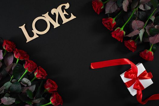 Red roses flowers with wooden word LOVE on black background with place for text. Romantic Valentines holidays concept. Valentine's day greeting card.. Copy space. Still life. Flat lay