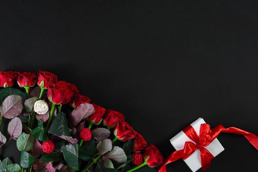 Red roses and white gift box with red ribbon on black background. Top view. Flat lay. Copy space. Still life