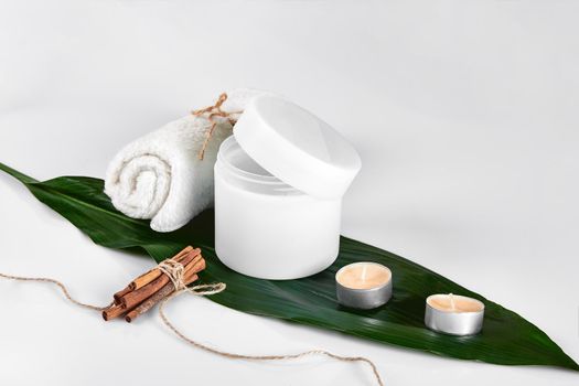 Cosmetic lotion with green leaf and candles. Skin care beauty treatment with jar of body moisturizer. White body lotion with big green leaf on light background.
